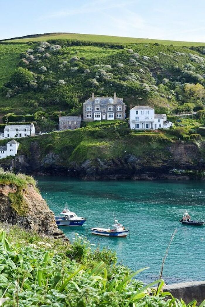 Coastal buildings with so much character overlooking a turquoise bay with boats, surrounded by lush green hills.