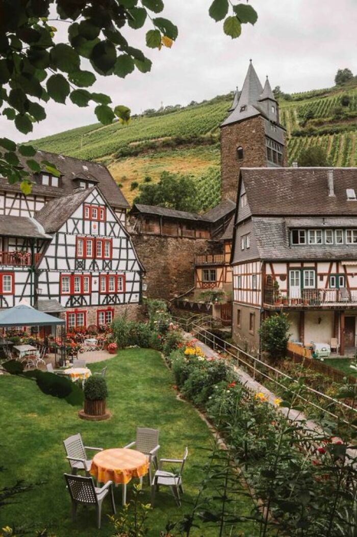 Traditional half-timbered buildings with character and a garden, nestled in a picturesque valley with vineyards.