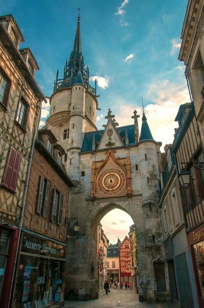 An ancient clock tower building with so much character, standing tall over a narrow cobblestone street.
