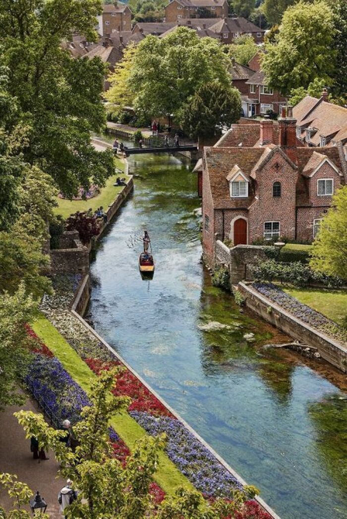 A charming riverside scene with a small boat on a clear canal, flanked by old brick buildings and lush greenery, embodying unique character.