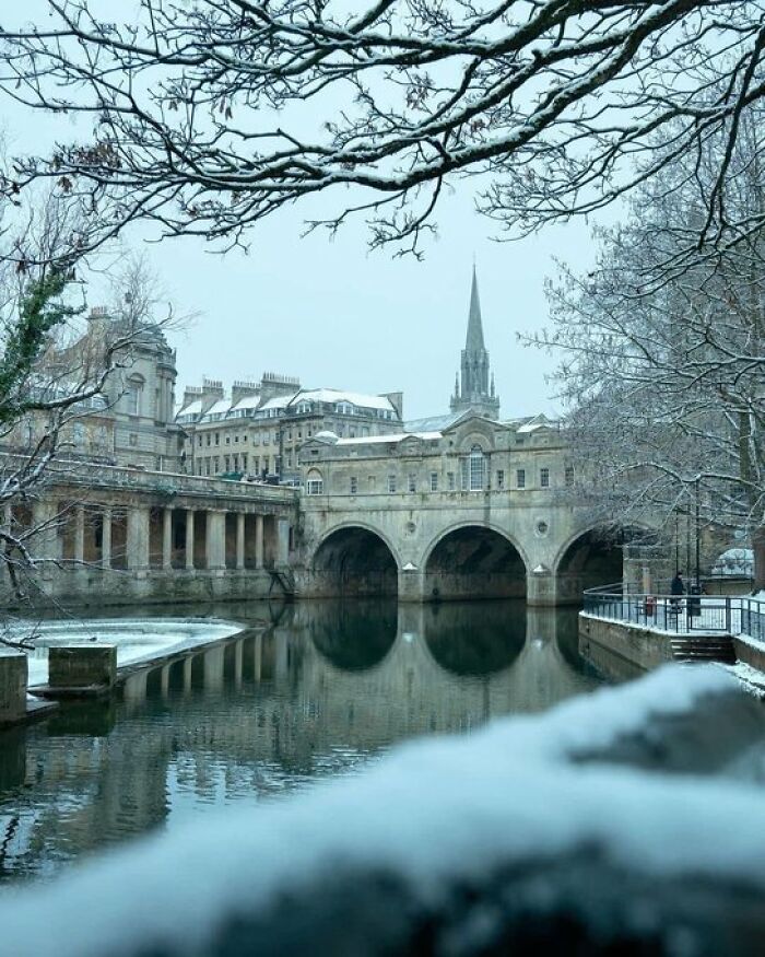 A snowy winter landscape featuring a historic bridge over a river, exemplifying buildings with so much character.