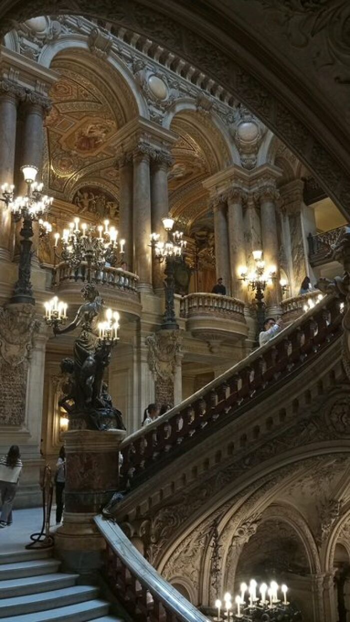 Grand interior of a historic building with character, showcasing ornate staircases, chandeliers, and classical columns.