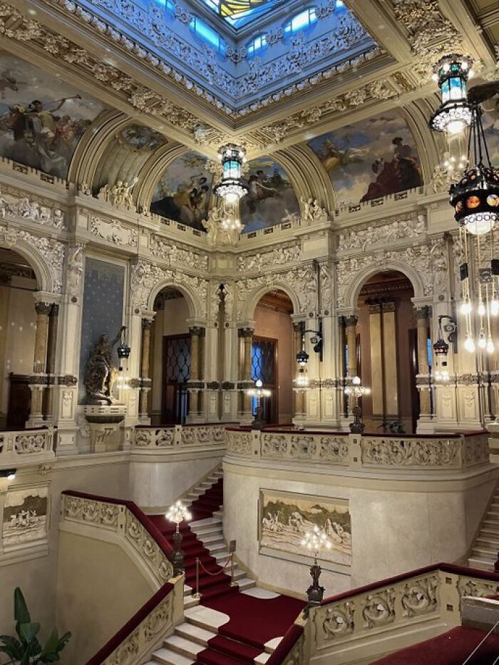 A grand hall with a sweeping staircase and detailed ceilings, showcasing buildings with so much character.
