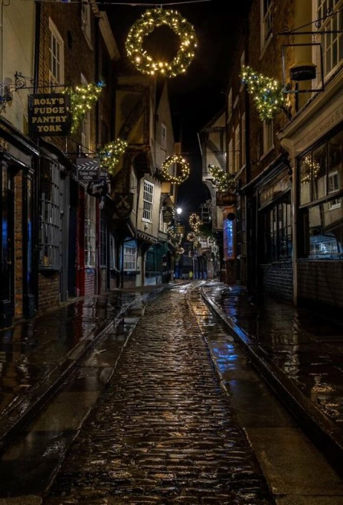A narrow cobblestone street adorned with Christmas lights, showcasing buildings with so much character at night.