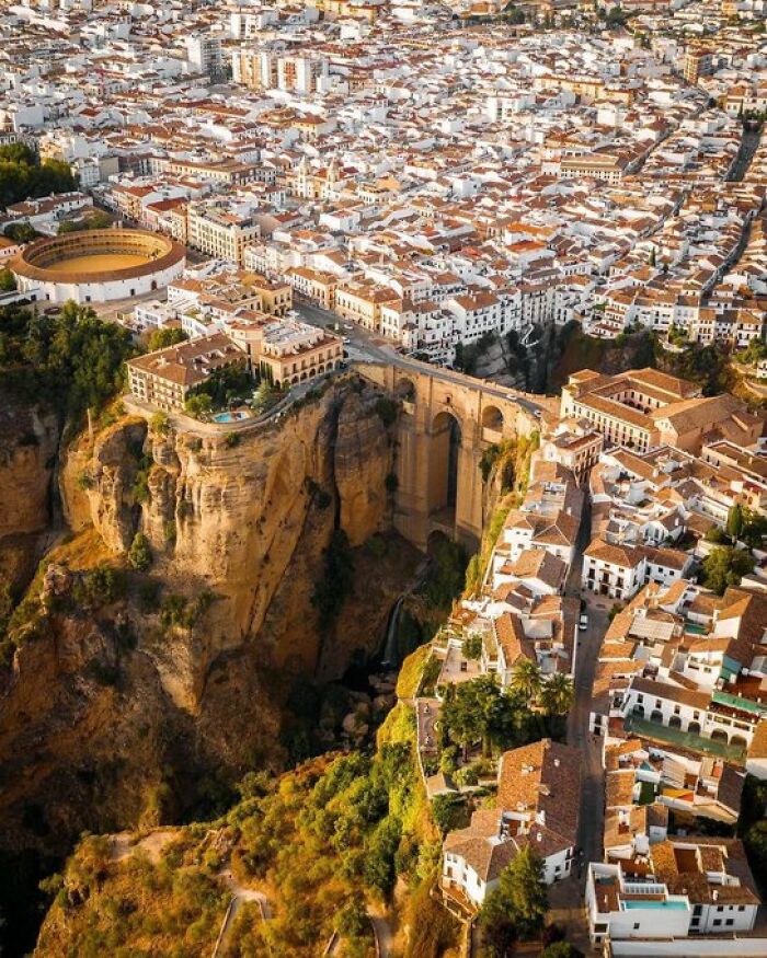 An aerial view of a Spanish town built atop a cliff, with many buildings and a bridge, showing unique character.