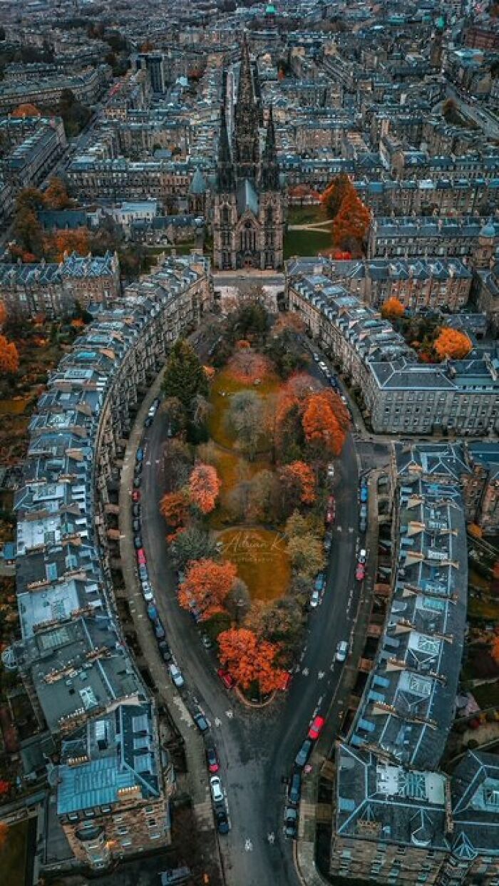 An aerial view of a city street with buildings forming an oval around a park with autumn trees, highlighting character.