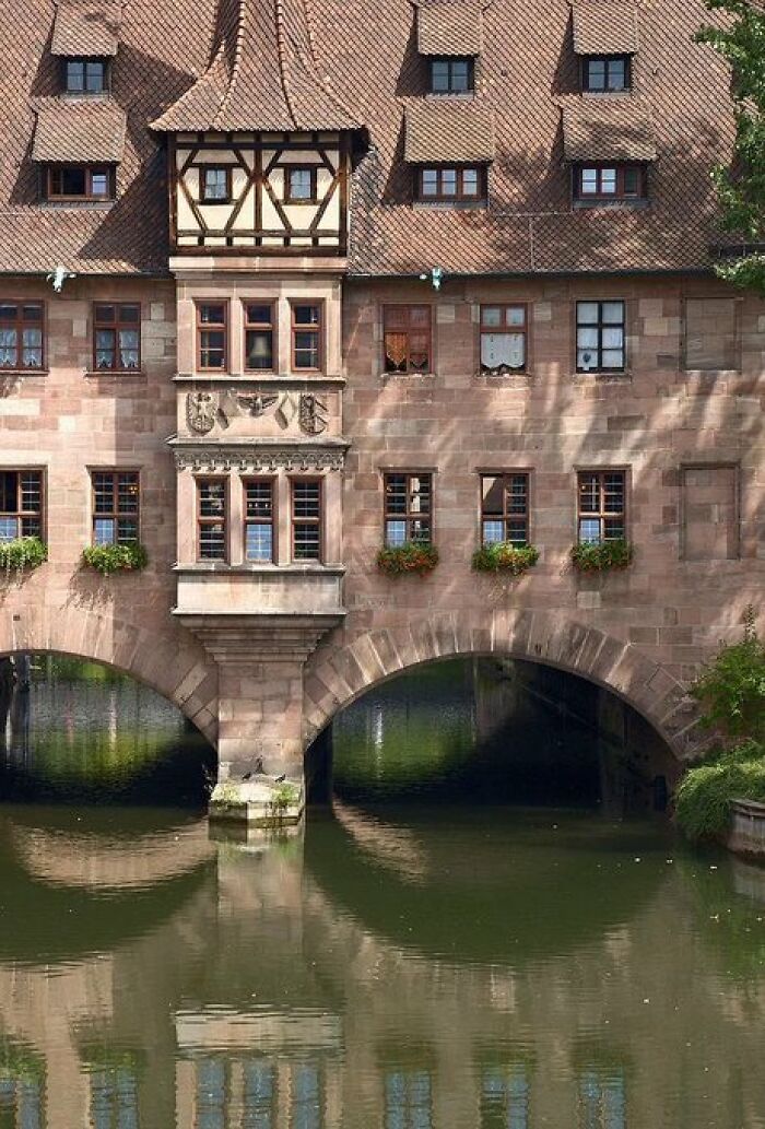Historical stone buildings with character spanning a river, featuring multiple windows and a unique architectural style.