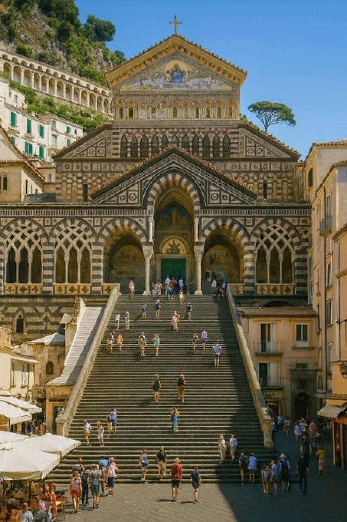 Tourists ascend a grand staircase to an ornate cathedral, an impressive building with historic architectural character.
