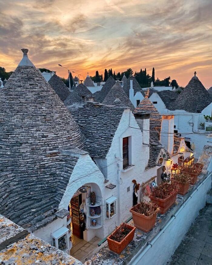 Quaint white buildings with conical roofs and warm lights glow under a vibrant sunset, showcasing charming architectural character.
