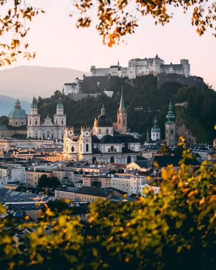 An aerial view of Salzburg, featuring numerous buildings with character, crowned by a grand fortress on a hill.
