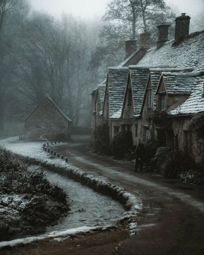 A mystical, fog-shrouded village with ancient stone buildings with character lining a winding, snow-dusted road.