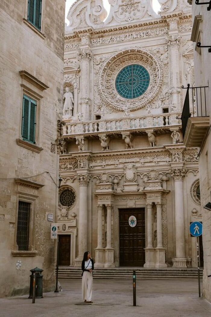 A woman stands before an ornate Baroque cathedral, a building with character, showcasing intricate carvings and a grand rose window.