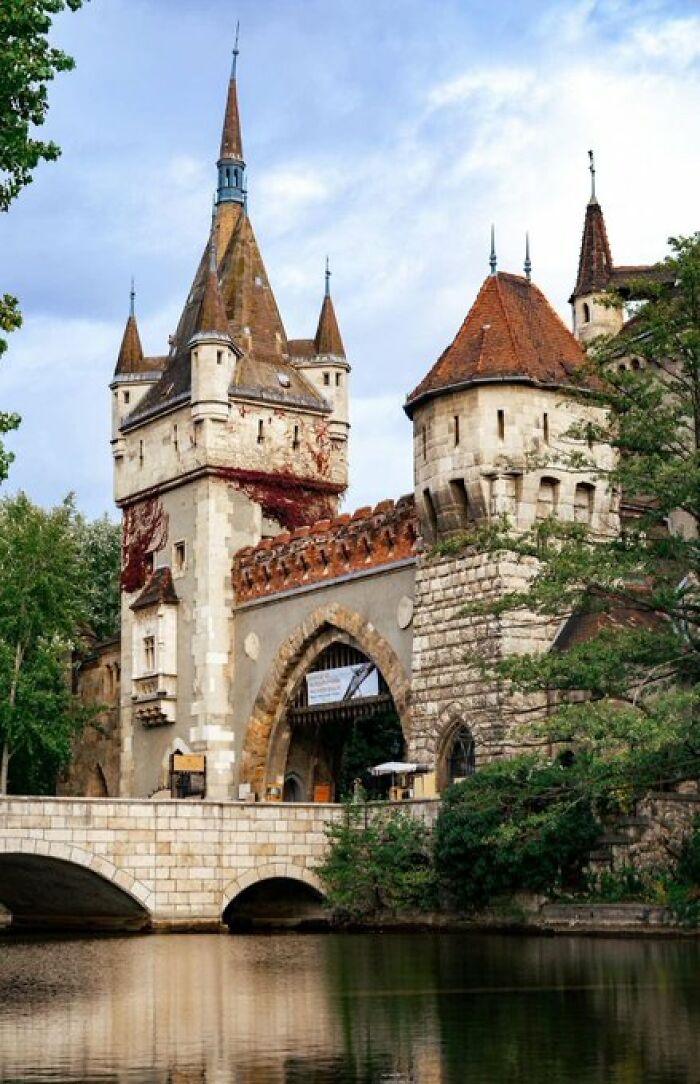A majestic castle, a building with character, rises above a tranquil moat with an arched bridge leading to its entrance.