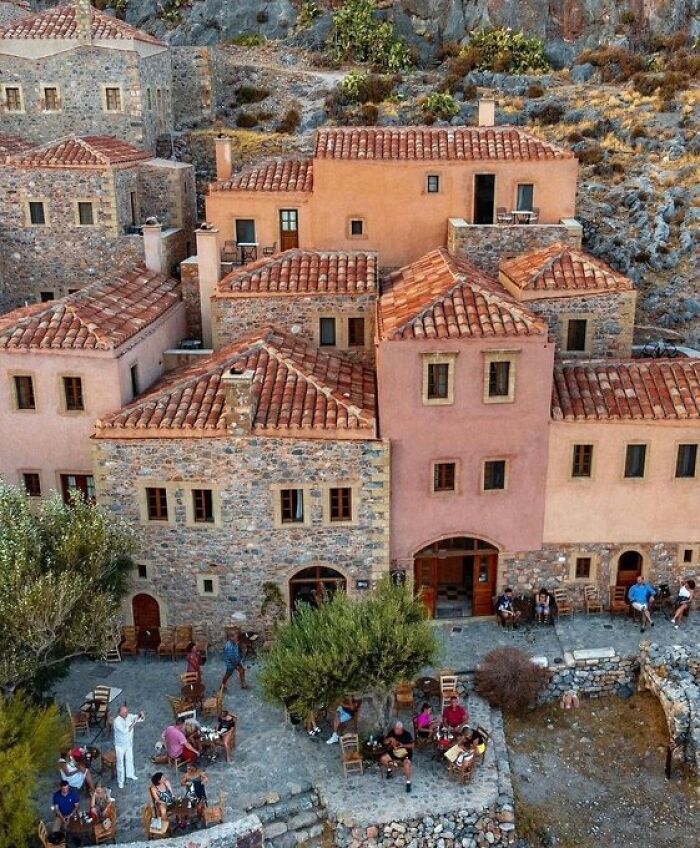 Stone and stucco buildings with character and red tile roofs built into a rocky hillside, featuring a lively outdoor dining area.