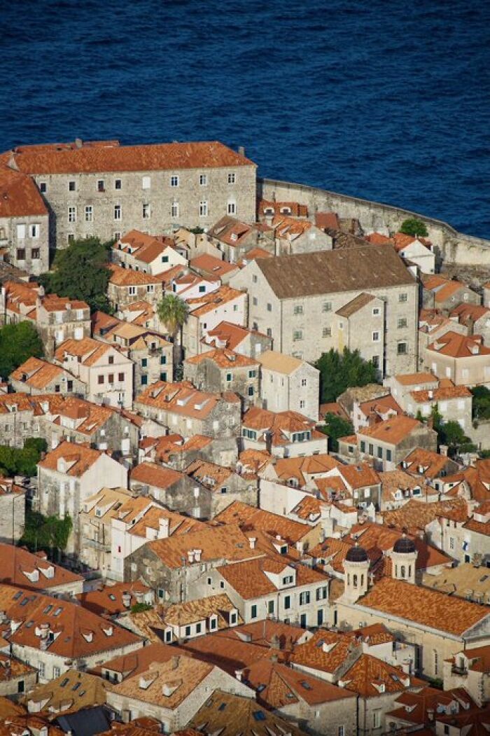 Aerial view of character buildings with red roofs by the sea, showcasing traditional architectural designs.