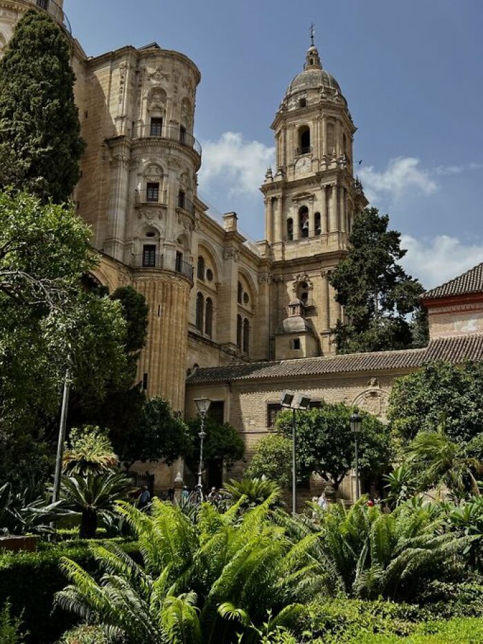 An ornate historical building with a tall bell tower and intricate architecture, surrounded by lush green gardens, displaying character.