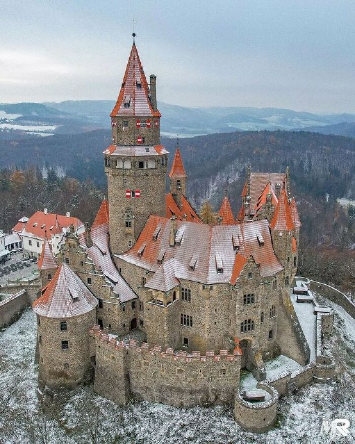 A majestic medieval castle with red roofs and stone walls, covered in snow, showcasing a building with character.