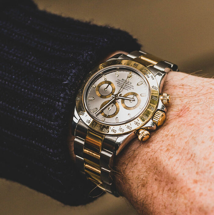 A close-up of a person's wrist wearing a two-tone gold and silver Rolex watch, emphasizing the luxury item.