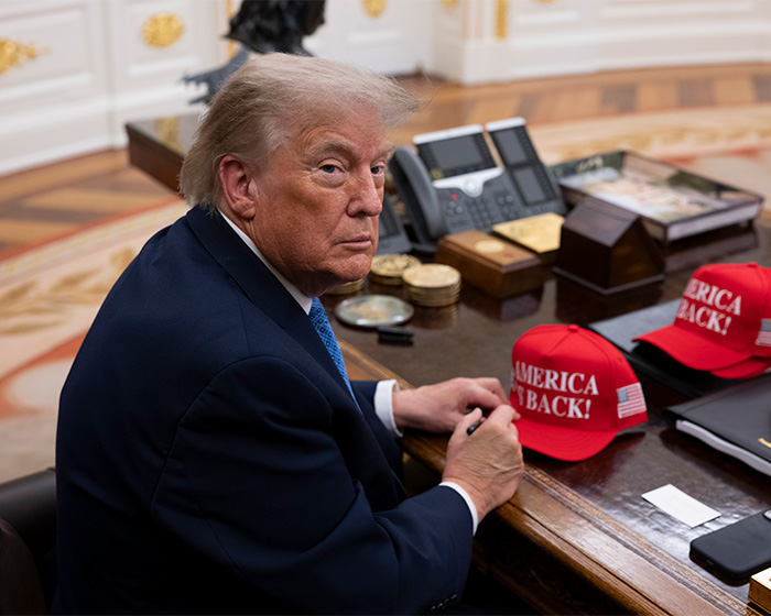 Donald Trump at his desk with America is back hats. Trump's comments about his assistant spark scrutiny.