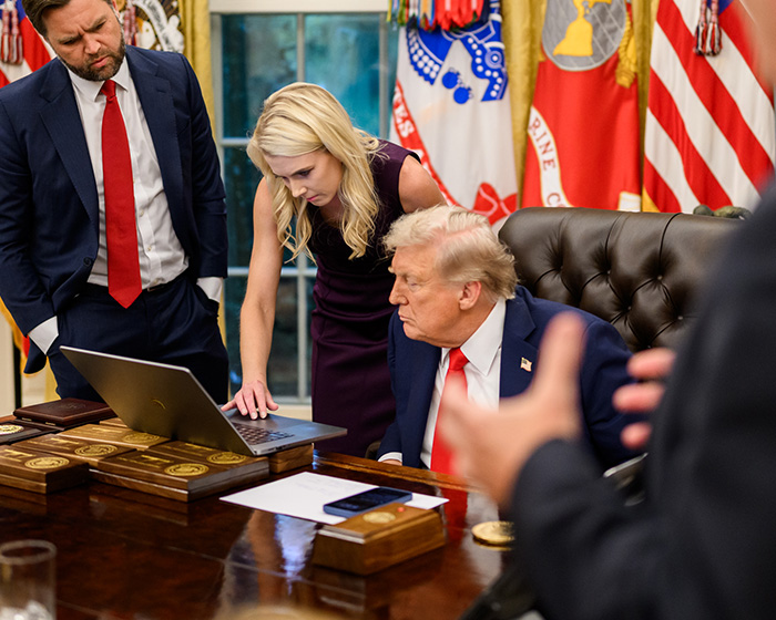 Female assistant showing something on a laptop to Trump, with a male aide beside her. Trump's comments.