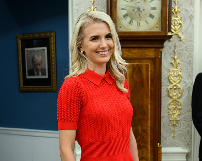 Smiling female assistant in a red dress with a clock and framed portrait in the background. Trump's comments.