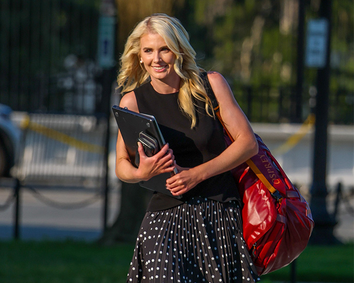 Natalie Harp smiling and walking outdoors, carrying a laptop and a red bag, amidst the Trump scandal. Natalie Harp smiling and walking outdoors, carrying a laptop and a red bag, amidst the Trump scandal.