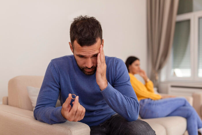 A man looking distressed while holding a wedding ring, contemplating signing divorce papers.
