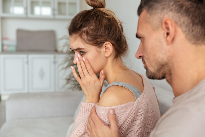 A woman crying while a man comforts her by placing a hand on her shoulder. They are dealing with emotions, perhaps related to divorce papers.