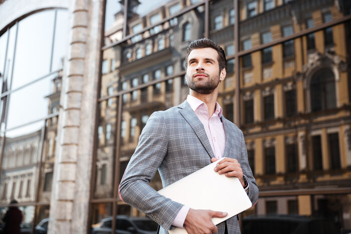 A dapper businessman holding a laptop, representing men's careers and personal lives amidst divorce.