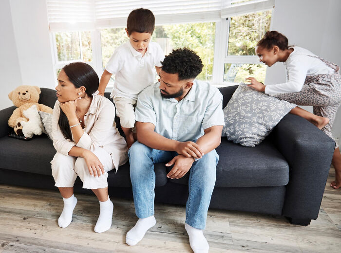 A family with two children sitting on a couch, appearing unhappy. The parents face away from each other, considering divorce papers.