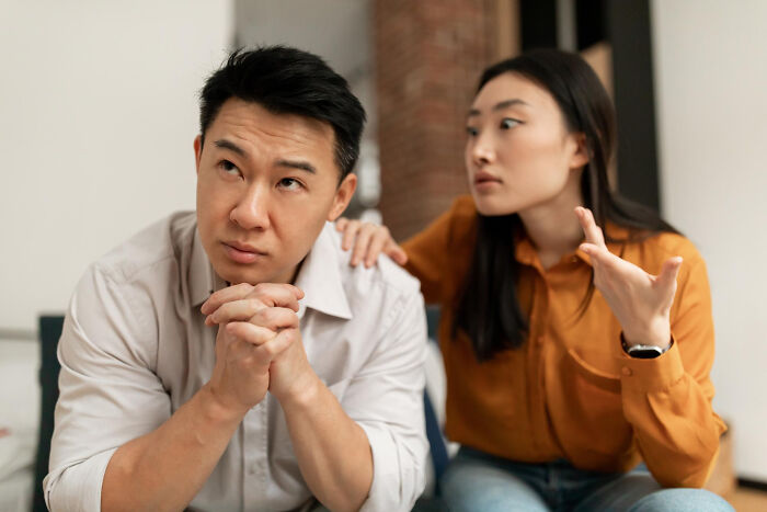An Asian couple arguing, where the man looks away, hinting at divorce papers and fighting.