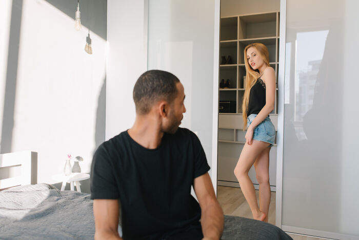 A man sitting on a bed looking at a woman standing in a doorway. Their interaction suggests deep honest thoughts about divorce papers.