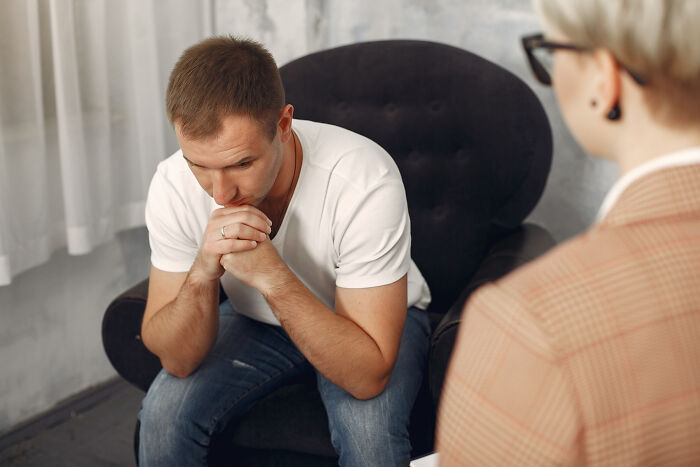 A man looking down in a therapy session, considering divorce papers or fighting less.