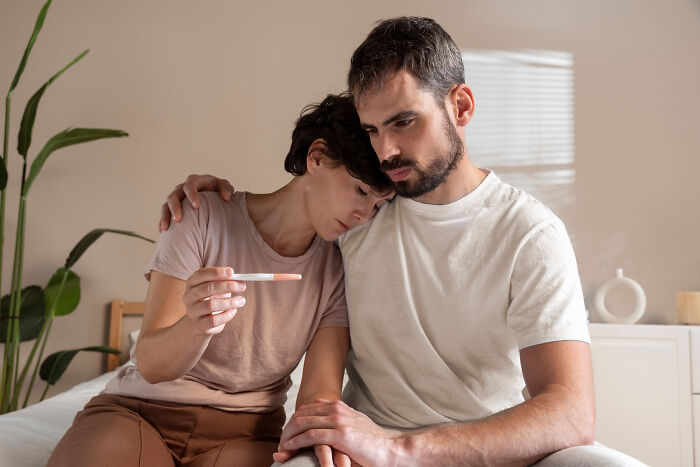 A sad couple looking at a pregnancy test, possibly fighting or discussing divorce papers.