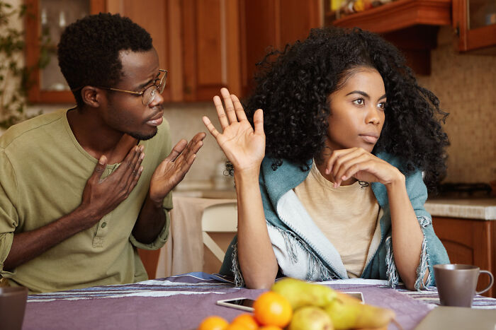 A couple arguing in a kitchen, with the woman holding up a hand, possibly discussing divorce papers.