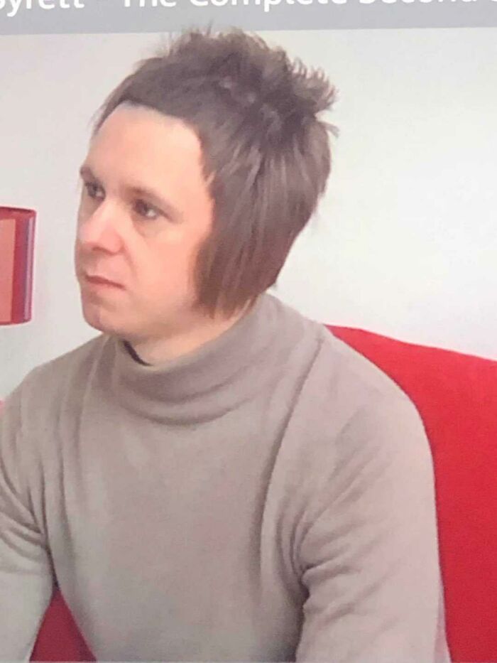 A man with a unique hairstyle and a turtleneck, an example of dry British humor.