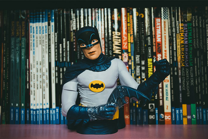 A Batman toy action figure stands in front of a shelf filled with Batman comic books. A Batman toy action figure stands in front of a shelf filled with Batman comic books.