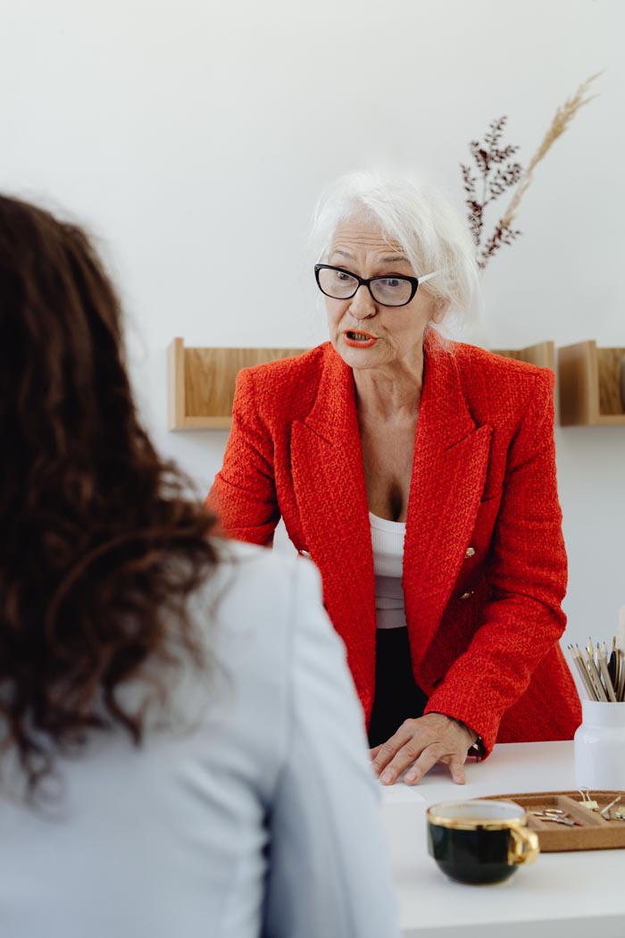 An older woman in a red jacket looking angry while speaking to someone, representing challenging MILs.