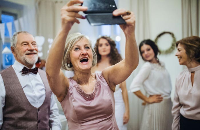An older woman happily taking a selfie at an event, surrounded by family, contrasting with bad MILs.