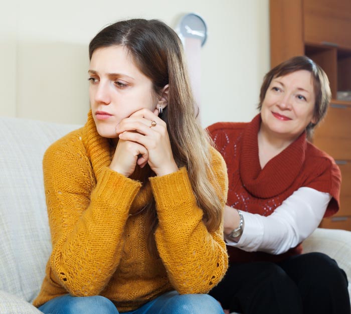 A young woman looking sad while an older woman smiles, illustrating difficult MILs.