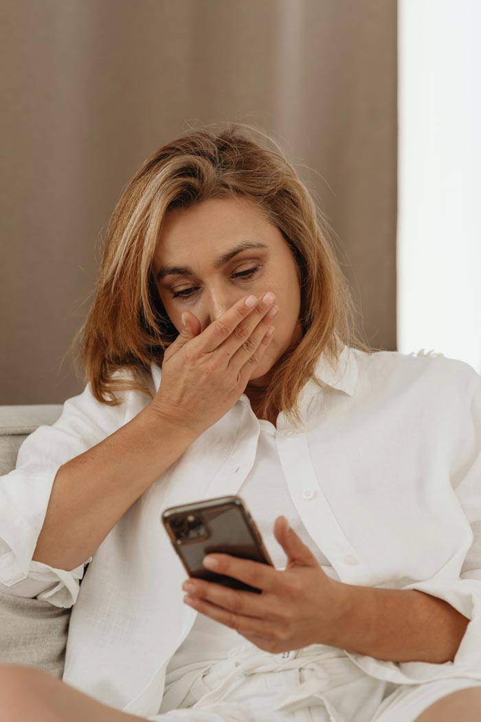 A woman looking shocked at her phone, representing MILs you wouldn't wish upon your worst enemy.