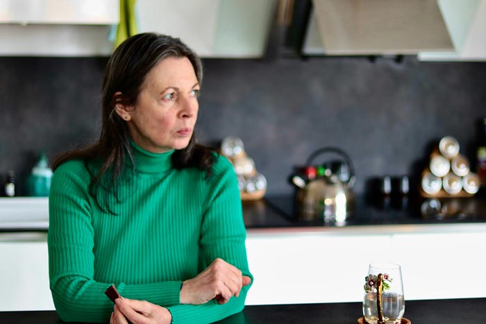 A woman in a green turtleneck looking worried in a kitchen, experiencing one of 53 MILs.