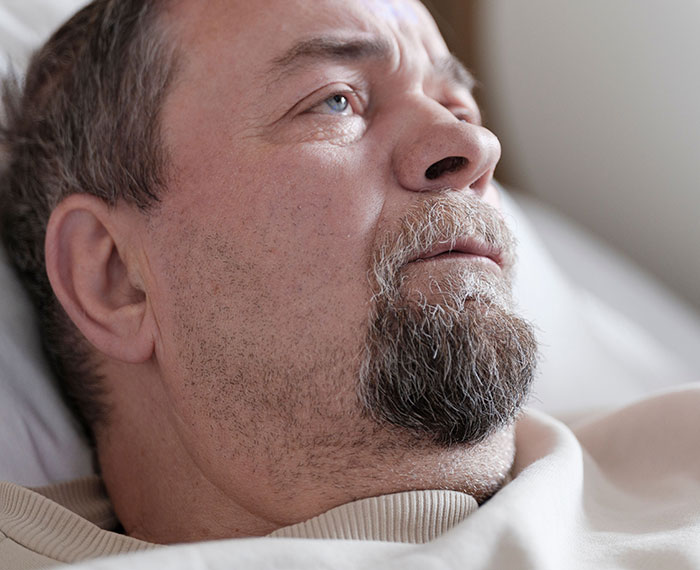 A thoughtful male patient in a hospital bed, looking upwards, perhaps contemplating weird things unprovoked.