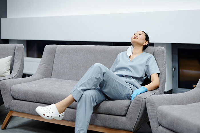 A tired nurse relaxing on a couch, reflecting on long shifts where patients said weird things.