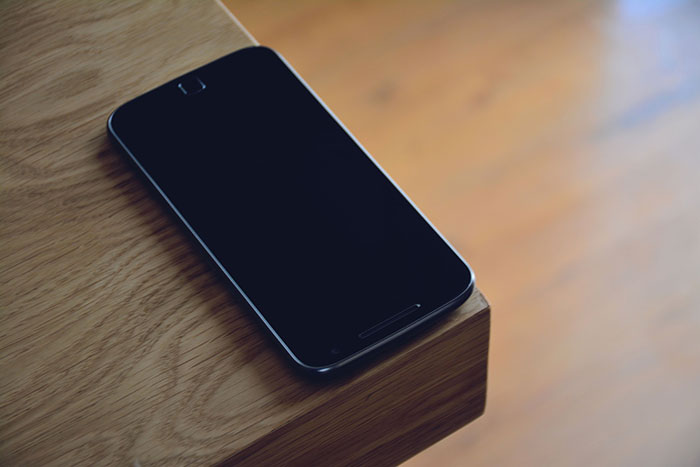 A black smartphone resting on the corner of a wooden table. Patients said weird things.
