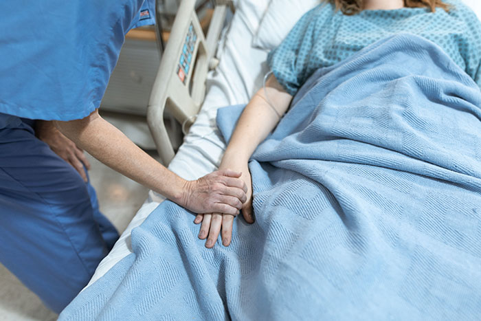 A nurse holds the hand of a patient in a hospital bed, providing comfort and support for patients.