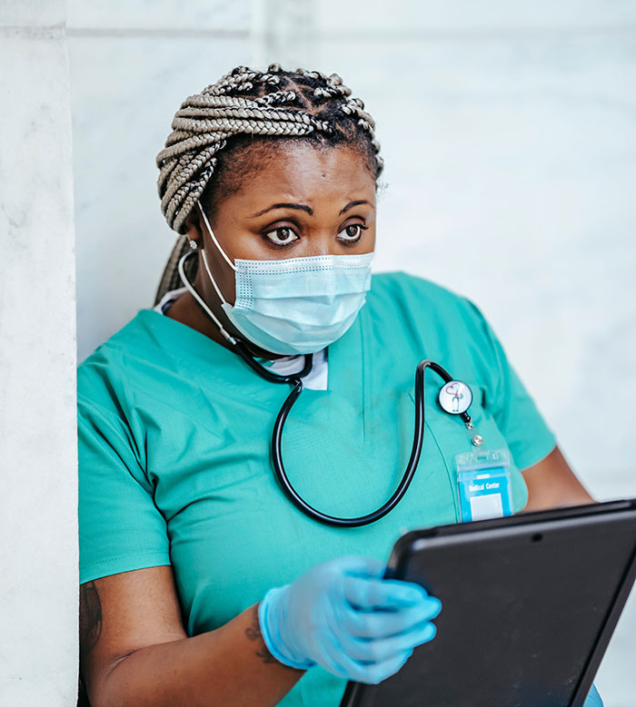 A Black nurse wearing a mask and gloves, looking surprised while holding a tablet, reflecting patients said weird things.
