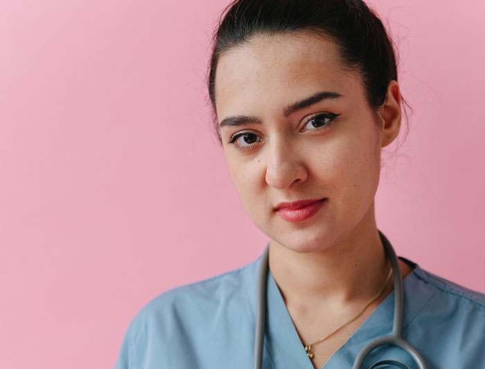 A nurse in blue scrubs with a stethoscope, looking at the camera, conveying patients said weird things.
