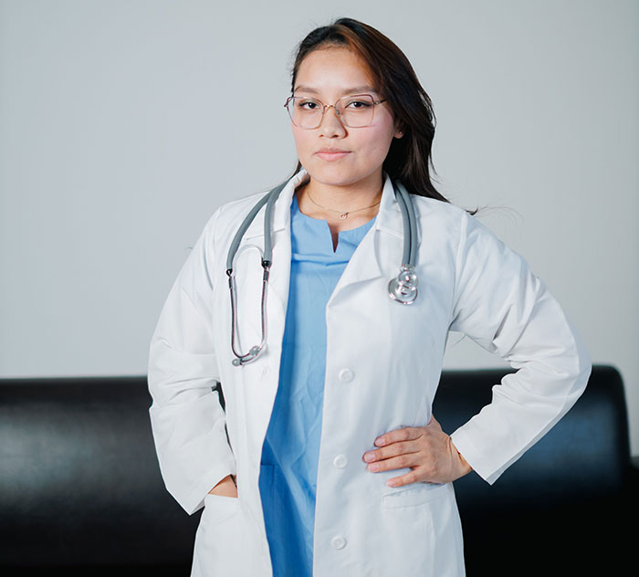 A female medical professional in a white lab coat and scrubs, confidently posing. Patients said weird things.