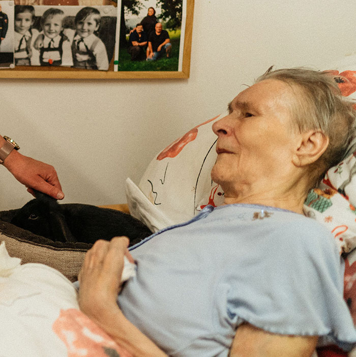 An elderly patient in bed, with a hand petting a dog, possibly sharing something weird and unprovoked.